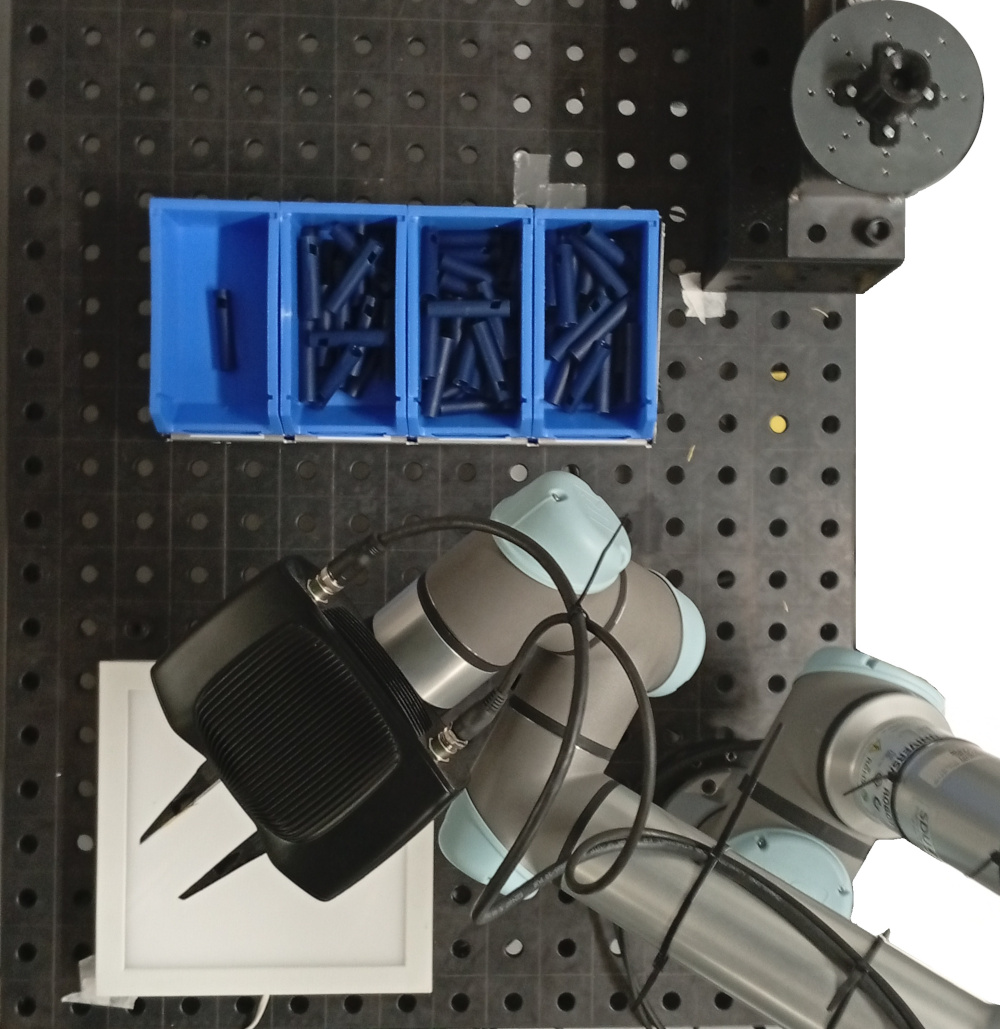 Figure 4: The workcell used for experiments. The overhead camera for in-hand inspection is placed directly above the white backlight. The leftmost bin is used for re-orientation tray. Top right is the re-orientation fixture used in [24].